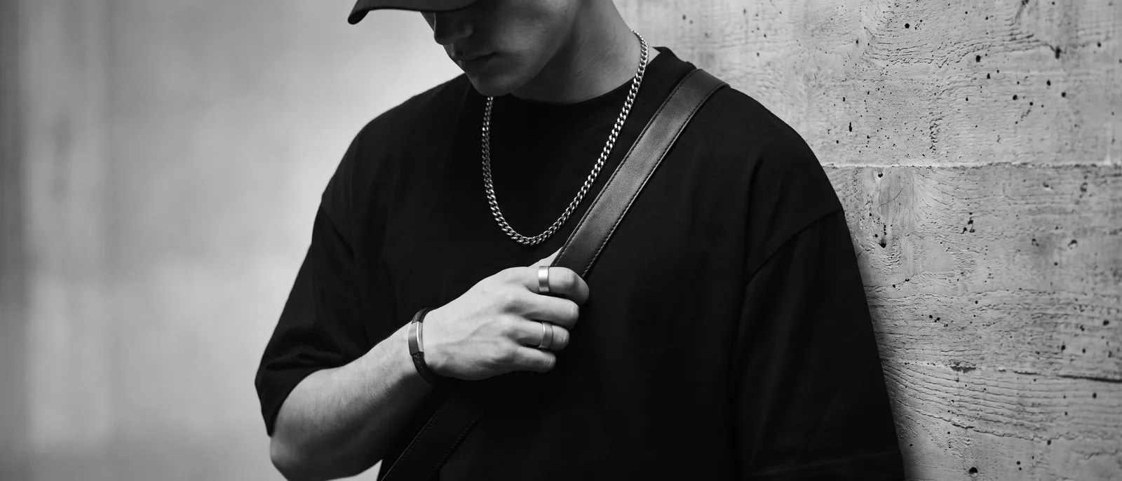 Accessories: a close editorial crop of a silver chain, rings, a bracelet and a leather bag strap over a black t-shirt
