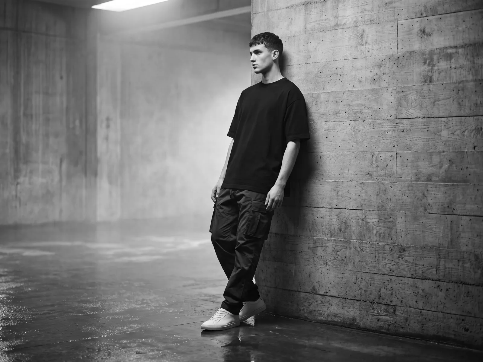 Essentials: a model in an oversized black Dangerous Street t-shirt and cargo trousers, standing against a raw concrete wall